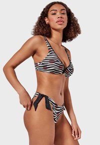 Bikini a rayas blancas y negras con acentos rojos, que presenta un diseño de cuello en V, lados ajustables con lazo y una tela suave y texturizada.