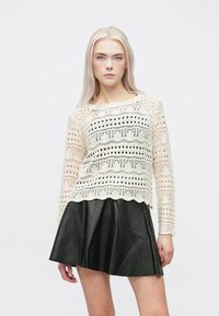 Maglione all'uncinetto color crema con motivo aperto e orlo a onde, abbinato a una gonna svasata in pelle nera. Maniche lunghe e vestibilità rilassata.