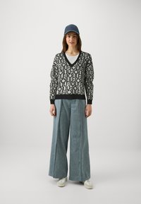 Maglione oversize nero e crema con motivo, colletto a V, abbinato a jeans a gamba larga blu chiaro e sneakers bianche, completato con un berretto blu.