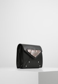 Borsa a tracolla in pelle nera con una patta argentata testurizzata, decorata con borchie argentate e un design geometrico. Forma angolare con una silhouette strutturata.