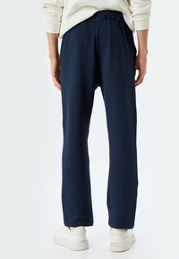 Pantalones tejidos en color azul marino con acabado texturizado, corte holgado, cinturilla elástica y bolsillos laterales, combinados con zapatillas blancas.