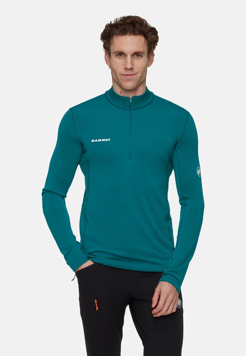 Türkisfarbener Fleece-Pullover mit langen Ärmeln, hohem Kragen und halbem Reißverschluss. Trägt das "Mammut"-Logo in Weiß auf der Brust und ein Emblem am Ärmel.