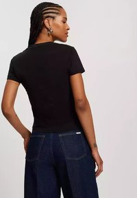 Czarna koszulka z krótkim rękawem o dopasowanym kroju, zestawiona z luźnymi niebieskimi dżinsami z widocznymi szwami i tylnymi kieszeniami.