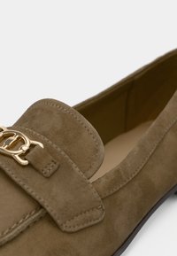Mocassins en daim beige avec un accent de boucle dorée, un bout arrondi et des détails cousus sur une surface supérieure lisse.