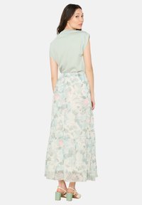 Svetlozeleno majica s kratkimi rokavi, v kombinaciji s plisejsko cvetlično maksi krilo v pastelnih barvah in z nežen teksturo. Masivni sandali z zelenimi petami.