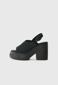 Sandales compensées noires avec une tige en tissu texturé, bout ouvert et une sangle ajustable à la cheville. Le talon épais ajoute de la hauteur.