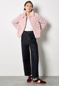 Giacca in pelliccia sintetica di un morbido rosa con colletto e righe orizzontali, abbinata a jeans in denim scuro a vita alta e sneakers bordeaux.