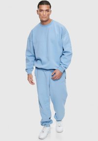 Lyseblå sweatshirt og matchende sweatpants sæt, lavet af blødt stof, med en afslappet pasform og ribbede manchetter, parret med hvide sneakers.
