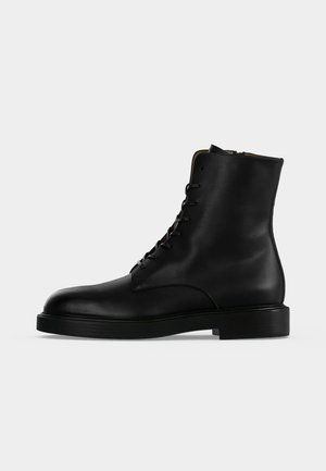 Bottine noire en cuir à lacets, semelle plate et bout arrondi, vue de profil sur un fond clair uni.