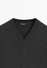 Maglione grigio scuro a V con colletto a costine e etichetta "Massimo Dutti Made in China" all'interno del collo.