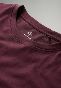 Burgundia puuvillane t-särk, millel on ümar kaelus. Seesmine krae kannab õmmeldud sildi "THE SET" ja "MADE IN BANGLADESH".