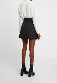 Gonna nera con un design a campana, abbinata a una blusa crema e stivaletti neri. Tessuto liscio con vita aderente e orlo ampio.