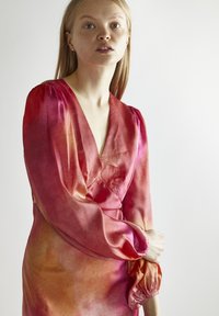 Silkkimekko syvällä V-aukolla, pitkät puffihihat ja gradienttikuosi vaaleanpunaisen ja oranssin sävyissä, pehmeä ja sileä rakenne.
