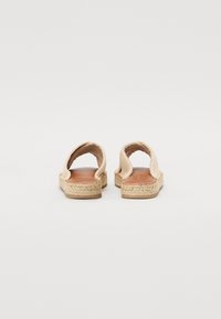 Beige espadrille sandaler med åpen bak, vevd jute-detaljering og en glatt brun skinnsåle. Flat såle for komfort og stabilitet.