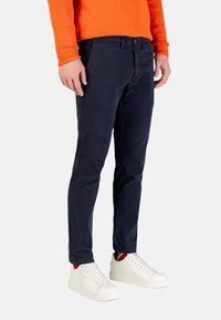Pantaloni chinos di cotone blu navy a vestibilità aderente, con chiusura a cerniera, tasche laterali e una texture liscia. Abbinati a sneakers bianche.