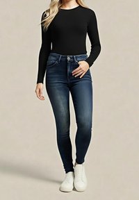 Top negro de manga larga combinado con jeans ajustados de talle alto en azul oscuro y zapatillas blancas. El conjunto presenta un diseño entallado y una textura suave.