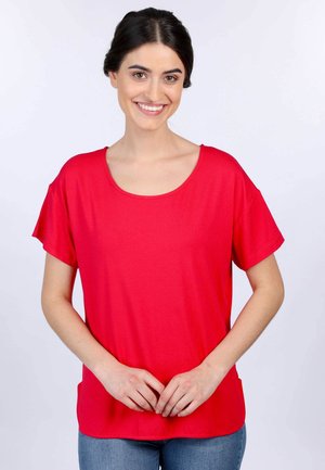 Rotes T-Shirt mit kurzen Ärmeln und Rundhalsausschnitt, glatter Textur, lockerer Passform und Seitentaschen, kombiniert mit blauen Jeans.