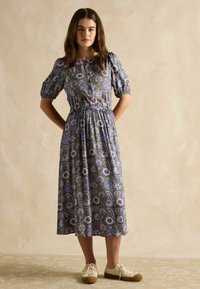 Blumengemustertes Midi-Kleid mit Puffärmeln, tailliertem Schnitt und grünem Hintergrund. Kombiniert mit cremefarbenen Schnürsneakern.