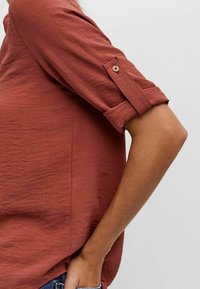 Rostfärgad blus med mjuk, strukturerad tyg, rullade ärmar med knappdetalj och avslappnad passform.