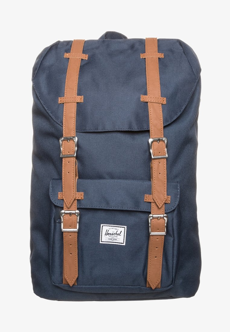 Sac à dos bleu marine avec des sangles en cuir brun et des boucles en argent, poche avant et étiquette de marque Herschel blanche.