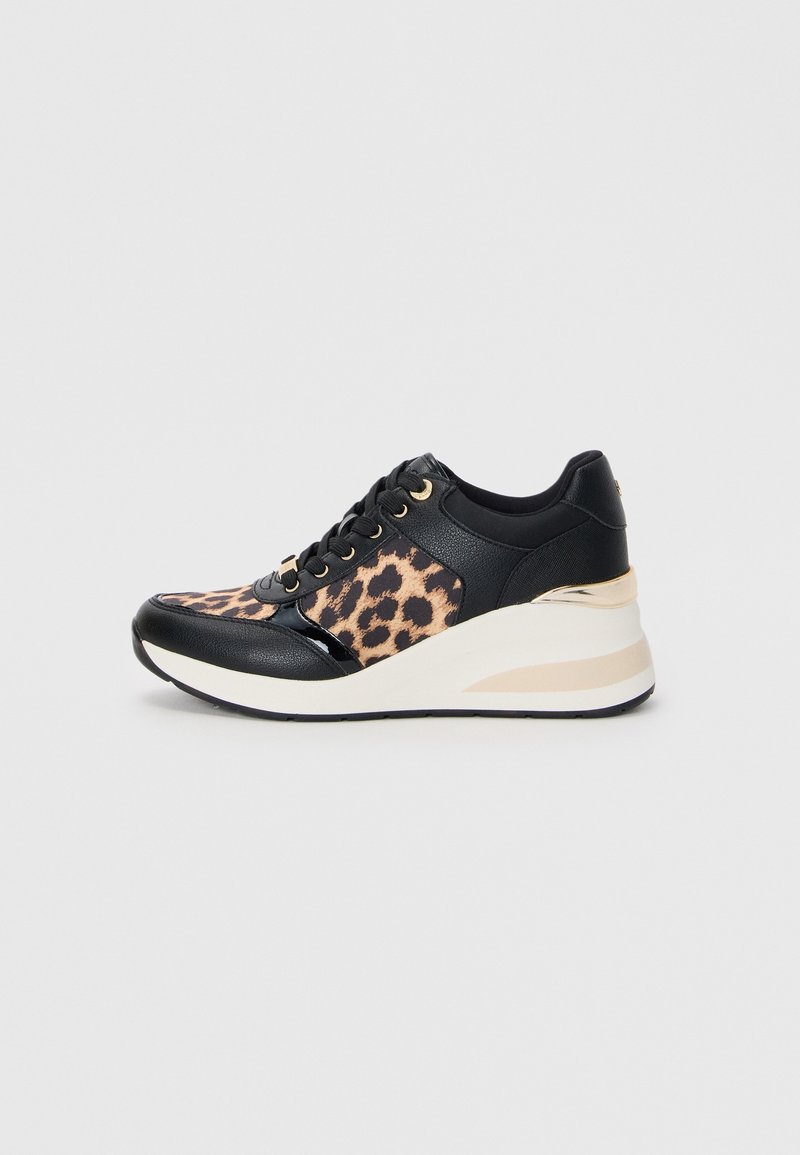 Baskets compensées noires avec panneaux en tissu imprimé léopard, œillets dorés et semelle plateforme blanche avec accents beiges sur fond gris clair.