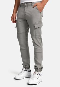 Graue Cargo-Hosen im Slim-Fit, mit Seitentaschen und elastischen Bündchen, kombiniert mit weißen Sneakern. Hergestellt aus strapazierfähigem Baumwollstoff.