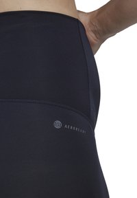 Leggings atletici blu navy realizzati in tessuto traspirante con una texture liscia, dotati di un logo discreto e cuciture piatte per il massimo comfort.