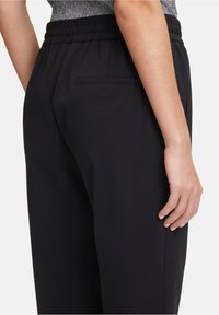 Pantalons de jogging noirs avec une texture lisse, une taille élastique, des poches latérales et un détail de poche arrière. Design décontracté pour le confort.