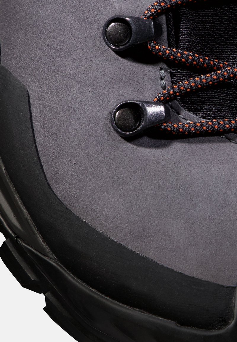Primo piano di un boot da trekking grigio con suola nera e lacci arancio-neri infilati in occhielli metallici.