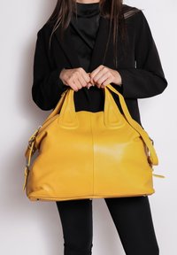 Borsa a tracolla gialla in pelle con una texture a granuli, manici superiori doppi e una tracolla removibile. Presenta un design spazioso e arrotondato.