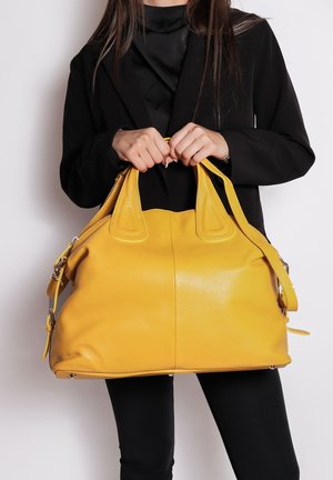 Sac à main en cuir jaune avec une texture granuleuse, deux poignées supérieures et une bandoulière amovible. Présente un design spacieux et arrondi.