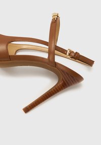 Sandale à talon haut en cuir brun avec un talon stiletto fin, une bride à la cheville et une boucle dorée. Présente une finition lisse et un design ajouré.