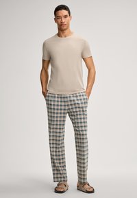 Beige t-shirt med korte ærmer, parret med ternede bukser i fløde, blå og grønne nuancer. Modellen har brune sandaler på. Minimalistisk design og afslappet pasform.