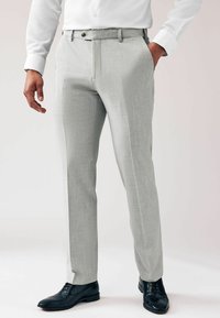 Pantalones ajustados de color gris claro, hechos de tela tejida, con frente plano, bolsillos laterales y un corte slim, combinados con zapatos de vestir negros.