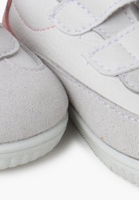 Scarpe per bambini bianche e grigio chiaro realizzate in pelle e camoscio, con cinturini in Velcro e una suola in gomma texture.
