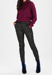 Blouse texturée bordeaux à manches bouffantes associée à un pantalon noir moulant à imprimé léopard et des bottines bleu marine.