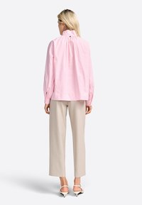Blusa de rayas rosa claro con cuello alto y espalda fruncida, combinada con pantalones de pierna ancha beige y tacones blancos con tiras.