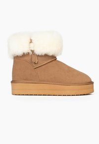Botas de tobillo en ante color marrón claro con un puño de piel de pelaje blanco suave, puntera redonda y suela de goma plana. Diseño simple con un mínimo de detalles.