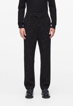Black textured trousers featuring a grid pattern, belt loops, and a straight leg design, paired with black shoes.