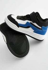 Baskets noir et blanc avec des accents bleus, dotées d'une semelle en caoutchouc texturé, d'une sangle Velcro et d'un dessus en matériau semblable à du cuir lisse.