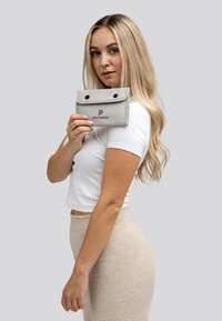 Grijze waterdichte pouch met drukknoopsluitingen en een logo. Zachte textuur, rechthoekige vorm, vastgehouden door een persoon in een wit shirt tegen een neutrale achtergrond.