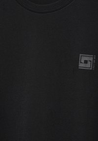 Sort bomulds-t-shirt med rund halsudskæring og et lille gråt logo foran. Stoffet har en glat tekstur.