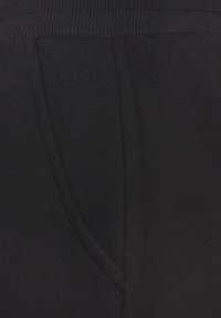 Crne trenirke izrađene od mekog, teksturiranog materijala, sa pojasom na vezanje i bočnom džepom sa detaljima šivanja.