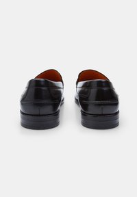 Mocasines de cuero negro con una superficie lisa, tacón bajo y punta redonda. El interior presenta un forro marrón en contraste con un sutil detalle de costura.