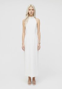 Valge varrukateta kleit kõrge kaeluse ja keha järgiva büstiga. Põrandapikkusega disain, sileda tekstuuri ja minimaalse detailidega, täiustatud läbipaistvate kontsadega.