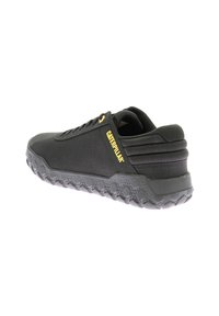 Zapatilla deportiva negra con un upper texturizado, suela gruesa con un patrón de panal y acentos en amarillo del logo.
