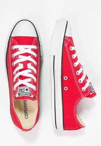 Sneakers in tela rossa con lacci bianchi, suola in gomma nera e punta bianca. Presentano il classico logo Converse All Star sulla linguetta.