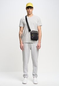 Grijze T-shirt en sweatpants met elastische boorden, gele pet en een kleine zwarte crossbodytas met een rits, met een logo en gele accenten.