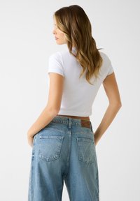 Biały krótki t-shirt z krótkimi rękawami w połączeniu z wysokim stanem jasnoniebieskich jeansów z denimu, z skórzaną naszywką na tylnej części pasa.