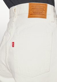 Närbild av vita Levi's jeans bakficka med röd Levi's etikett och brun läderpatch som visar varumärkesdetaljer.